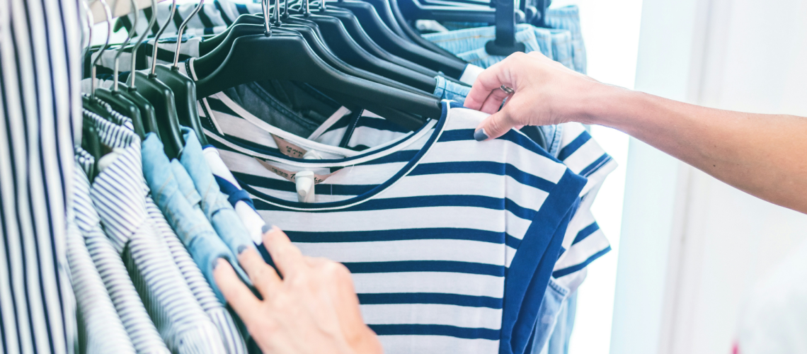 Person shopping for striped shirts on a clothing rack, highlighting ethical fashion and secondhand consumerism