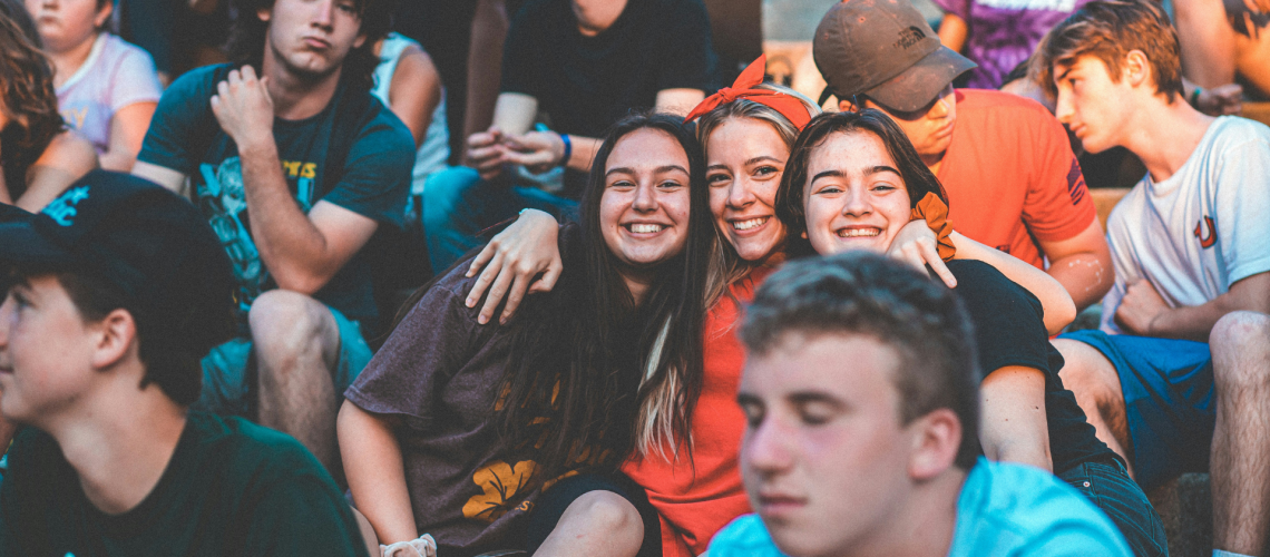 Group of teenagers gathered outdoors, with three girls smiling and hugging in the center, representing the importance of safe relationships and trusted community in preventing pornography and exploitation among youth.