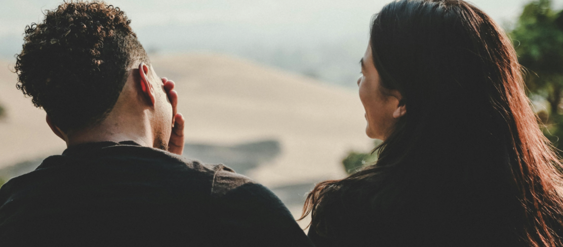 Man and woman sitting together outdoors, viewed from behind, capturing the quiet, complex dynamics that can exist in relationships affected by control, silence, or emotional tension