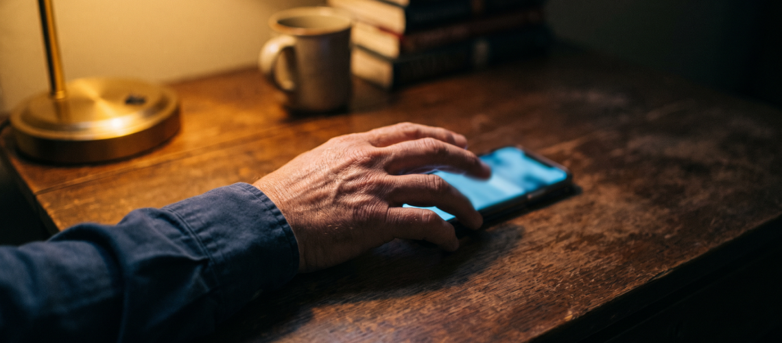A hand reaching for a glowing smartphone on a dark wooden table at night, symbolizing someone reaching out for human trafficking help resources