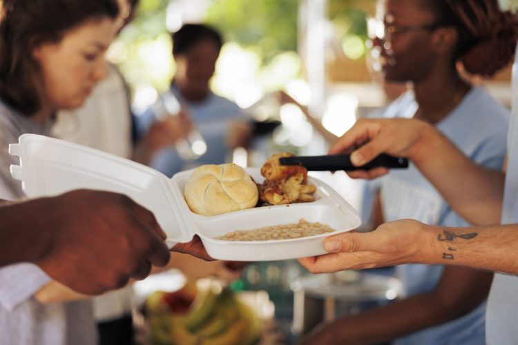 Photo focus on caucasian man serving bread, chicken and baked beans to poor and hungry african american person at non-profit food drive. Close-up of meal box from hunger relief team given to the needy.